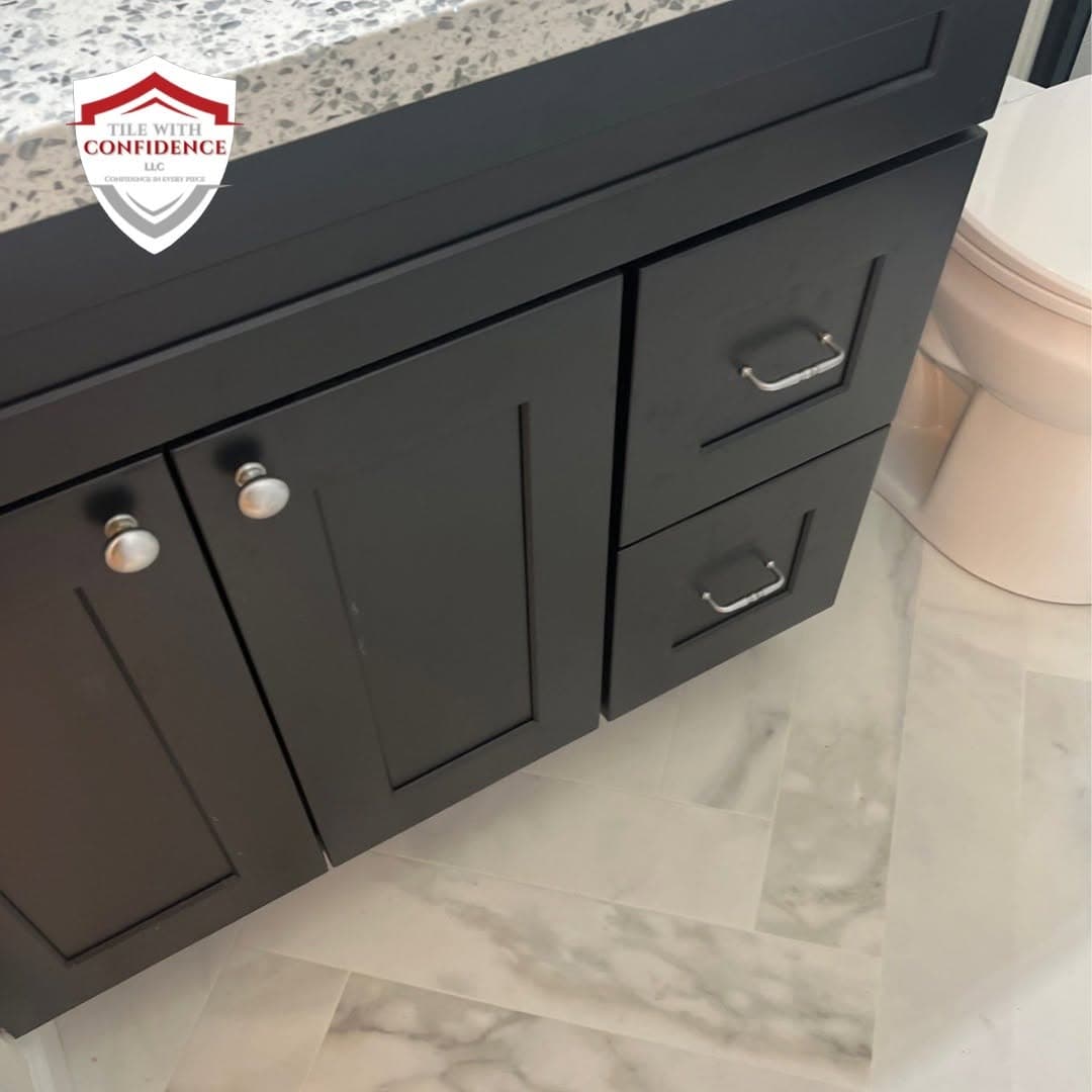 Bathroom tile flooring in marble-look porcelain running beneath a dark vanity cabinet
