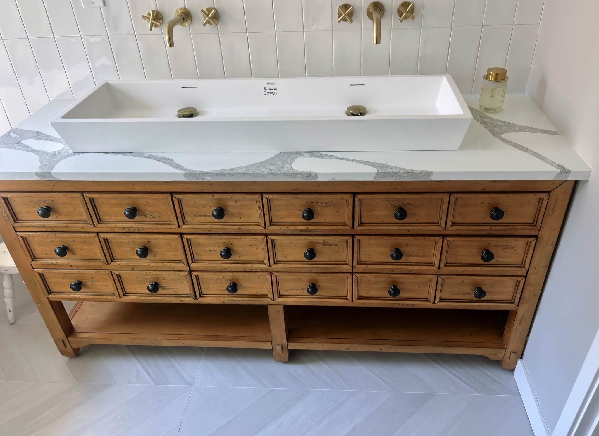 Residential tile detail showing vertical stacked tile with brass wall-mounted faucets above a trough sink