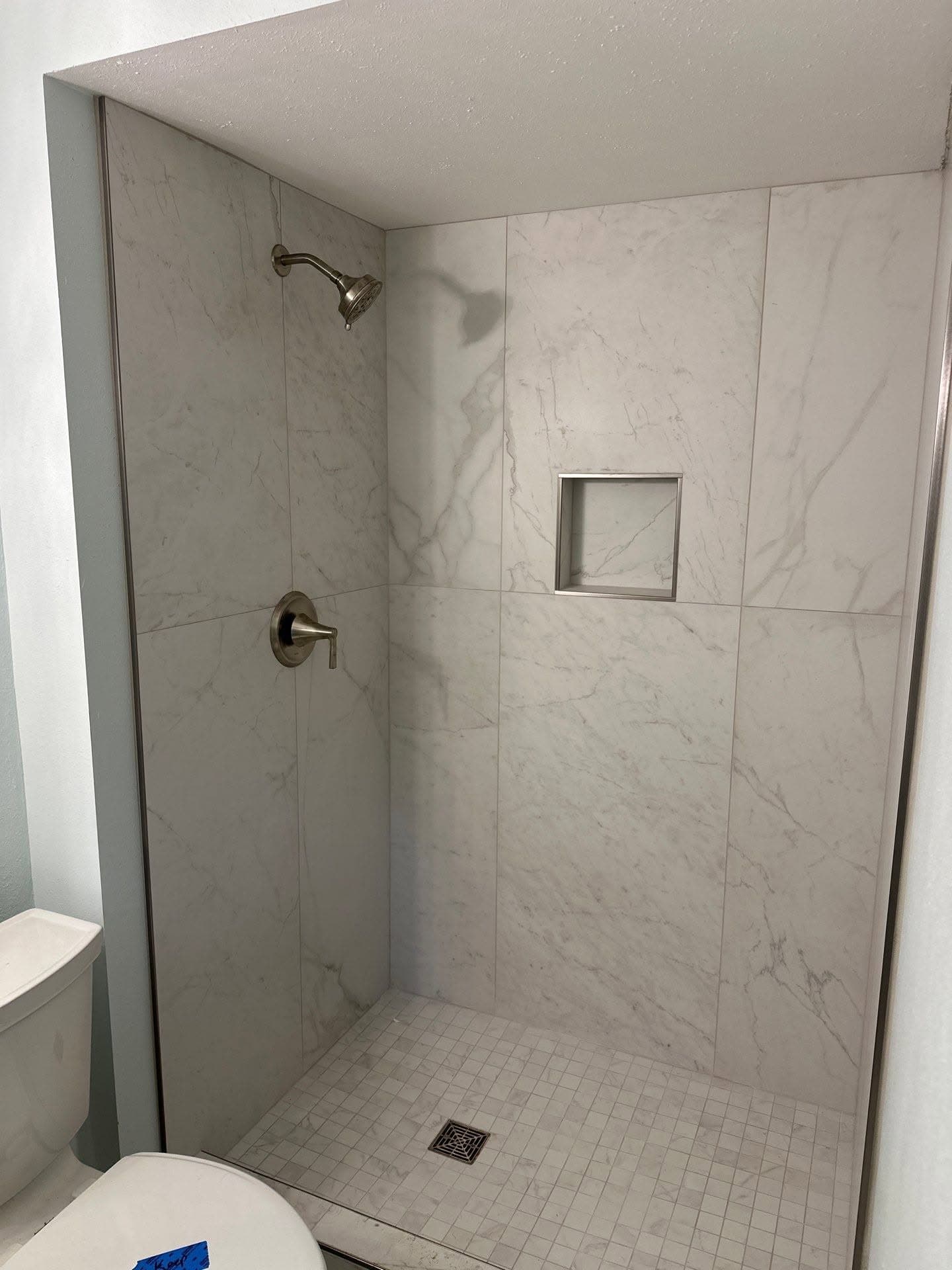 Shower niche and accent tile framed with metal trim in a marble-look tiled shower